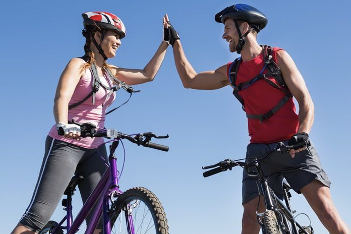 Fit cyclist couple standing at the summit high fiving
